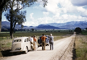 People standing on the road next to two Ford Prefect A493As, unspecified rural location, Victoria, Australia, 1956, Oceania