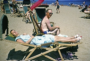 People sunbathing in deckchairs on the sandy beach of the Mediterranean Sea, Barcelona, Catalonia, Spain July 1958