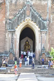 People visit a large temple with an imposing entrance and Buddha statue