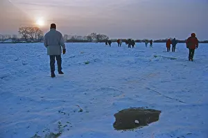 People walk across ice rink, sunset