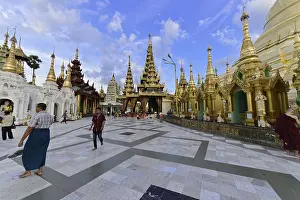 People walk on a sprawling square with pagodas and golden jewelry