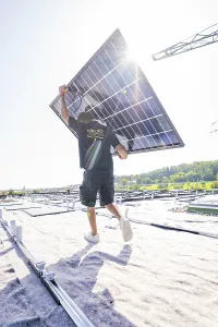 Person carrying solar panel under bright sun on a roof