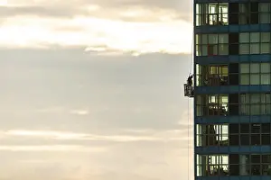 Person cleaning windows on a tall building against a cloudy sky in Toronto