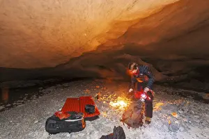 A person kneels by a campfire in a glacier cave