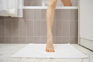 A person is stepping out of a bathtub onto a soft white mat
