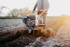 Person using a tiller on a farm field at sunrise