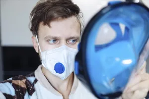 A person wearing a mask, holding a blue face shield