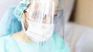 Person wearing medical attire looking thoughtful with full protective gear