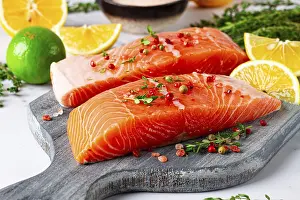 Two pieces of salmon fillet sit on a wooden cutting board