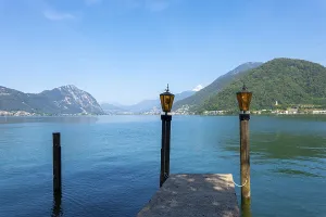 Pier with Lamps on Lake Lugano and Mountain Range in a Sunny Summer Day in Lugano