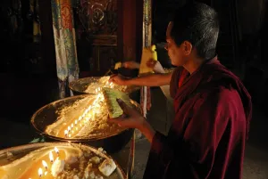 Pilgrim and Tibetan monks refilling the brass bow with yak butter