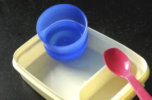 Plastic lunch box with spoon and blue glass on black background 18-June-2008