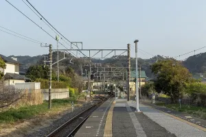 Platform and tracks through rural mountain landscape and arriving train at Hota Station in the evening light