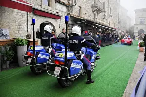Police motorcycles escort a classic car rally through the stone old town