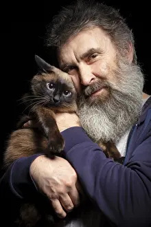 Portrait of an elderly man with a grey beard holding a cat