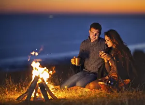 Portrait of the happy couple sitting by fire on autumn beach at the night