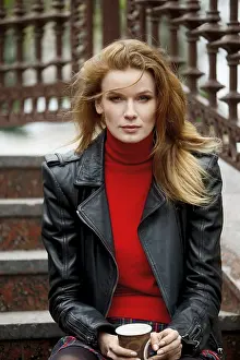 Portrait of red hair lady in leather jacket with cardboard cup in hand sitting on stairs