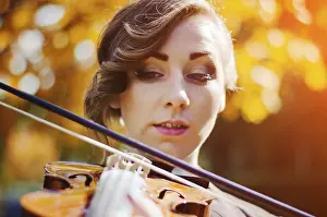 Portrait of smart girl with violin on hands outdoor in brown coat on autumn