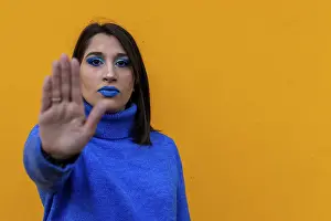 Portrait of a serious woman gesturing stop with his hand in front of a yellow background