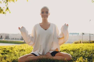 Portrait of young millenial european short haired woman doing yoga lotus asana on green grass meadow summer park sunset