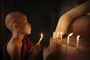 Portrait of young novice monk praying with candlelight inside a Buddhist temple