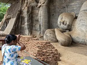Praying woman in front of a reclining Buddha statue