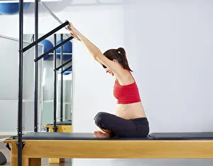 Category Oldtimer Prints: Pregnant woman pilates reformer forward push through exercise workout at gym