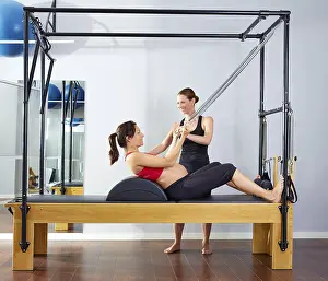 Pregnant woman pilates reformer roll up cadillac exercise with personal trainer