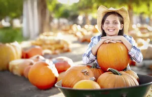 Pretty girl wearing cowboy hat enjoying the pumpkin patch on a sunny fall day