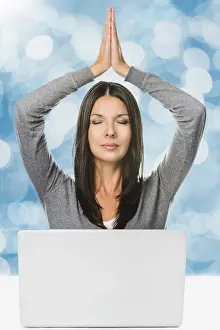 Pretty Long Hair Young Woman Meditating with Hands Over the Head and Closed Eyes In Front of a Laptop computer