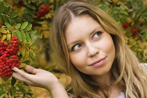 Pretty young woman touching ashberries in an autumn park