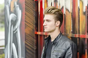 Profile of attractive blond haired young man standing against graffiti wall