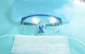 Protective glasses and a surgical mask placed on a blue surface