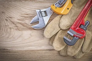 Protective gloves adjustable key monkey wrench pipe cutter on wooden board plumbing concept
