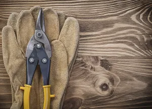 Protective gloves metal tin snips on wooden board construction concept
