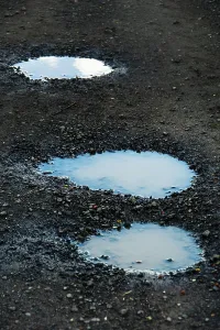 Three puddles on a gravel path mirror the overcast sky