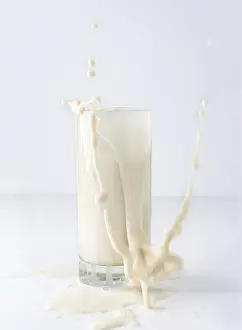 Quaint splash of vegetable milk in a tall glass on a white background