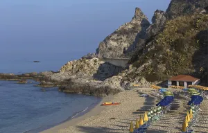 Quiet beach with parasols in front of a rocky coast and blue sea