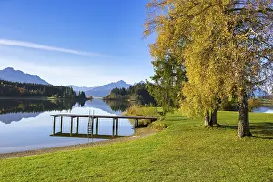 A quiet lake with a jetty, surrounded by autumnal trees and mountains under a clear blue sky