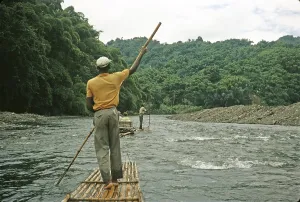 Rafting on the Rio Grande, Port Antonio, Jamaica, Caribbean 1970 Man pushes raft down river through tropical rainforest, Central America