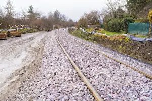 Railway tracks run curvy through a wooded landscape covered with gravel
