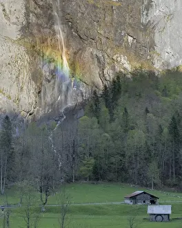 Rainbow-lit Waterfall Cascading Down Rocky Cliff Above Alpine Meadow in the Swiss Alps
