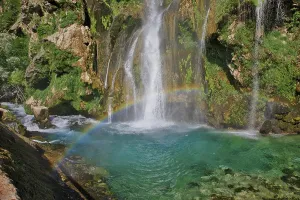 A rainbow stretches over a waterfall that flows into clear turquoise water