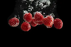 July 2024 Prints: Raspberries fall into water, black background