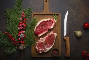 Two raw uncooked meat beef steaks on wooden cutting board with knife