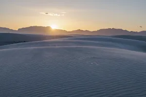 Rays of light over the mountains highlight windblown sand at sunset at White Sands National Park in Alamogordo