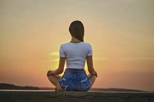 Rear view of a woman in meditation pose on the pier during summer sunset