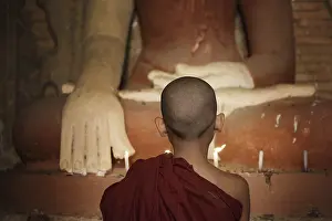 Rear view of young novice monk praying with candlelight inside a Buddhist temple