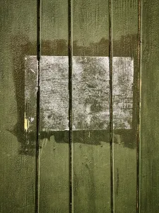 A rectangular patch on a green wooden surface shows faded remnants of a past application