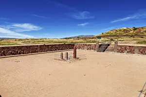 A rectangular square with stone pillars surrounded by ruins under a clear sky
